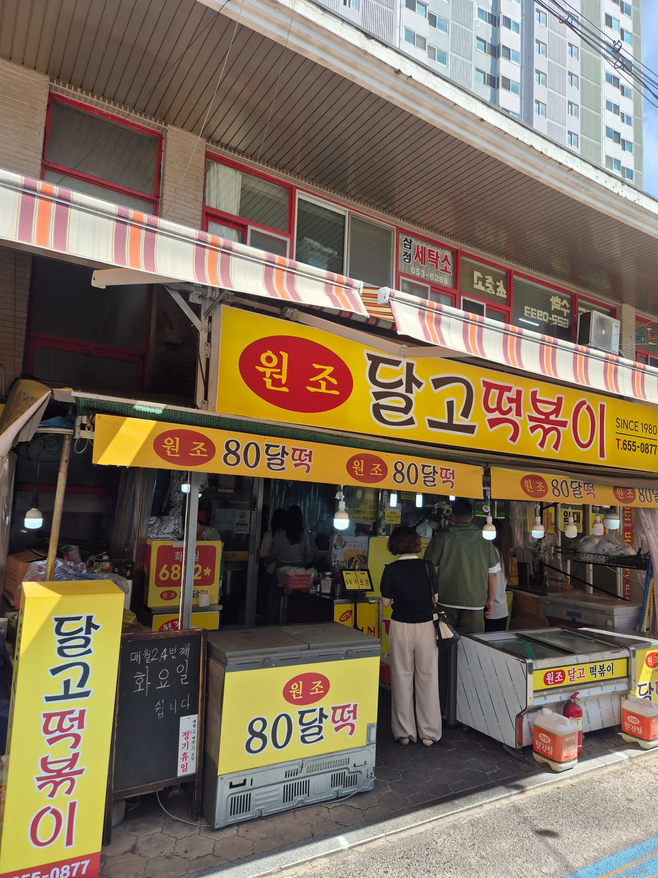 SINCE 1980 원조 80달떡 간판 아래 줄을 서서 기다리는 손님들의 다정한 뒷모습