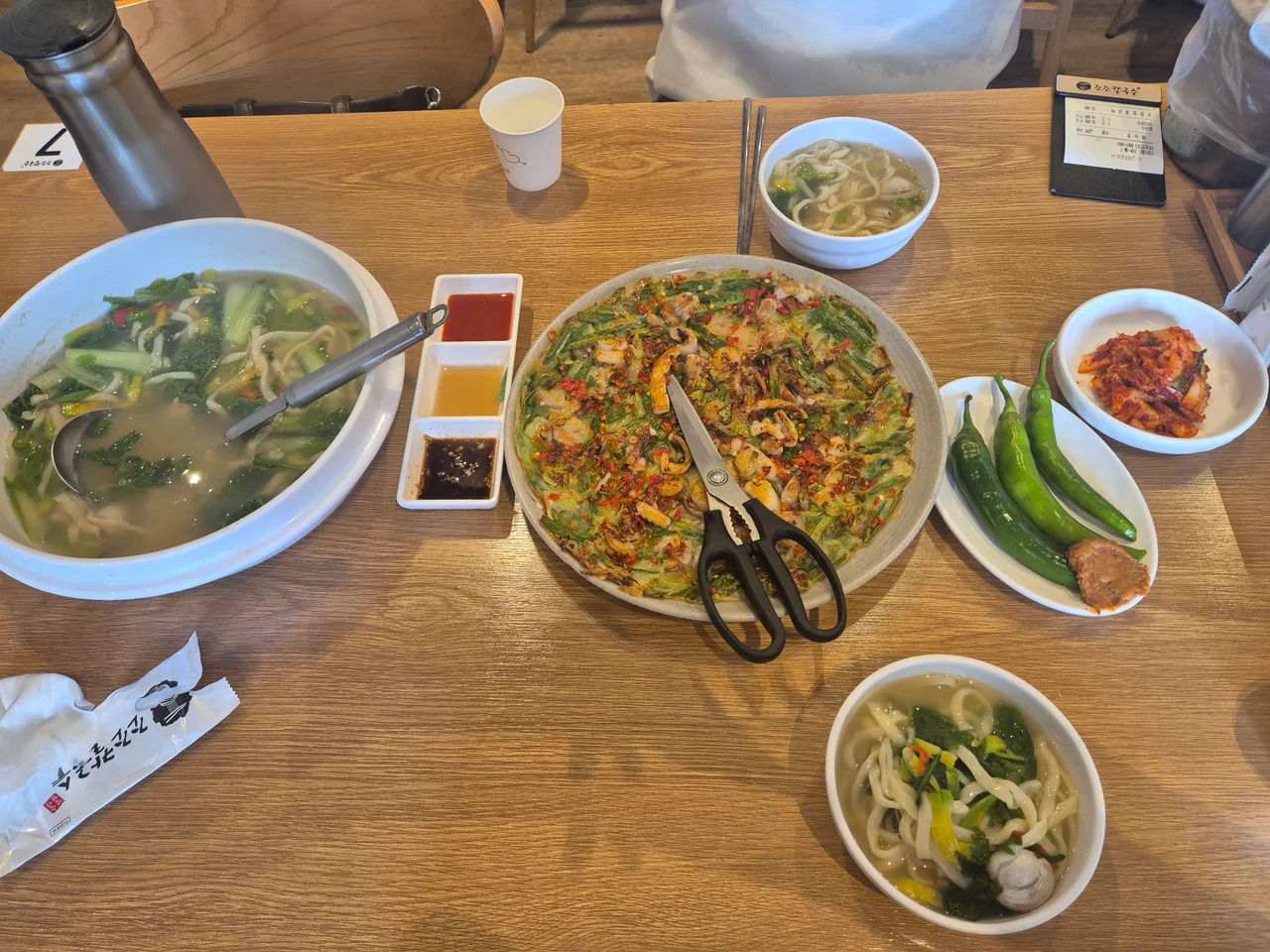 나무 테이블 위에 가득 차려진 조조칼국수의 풍성한 동죽칼국수와 낙지해물파전 한 상 차림