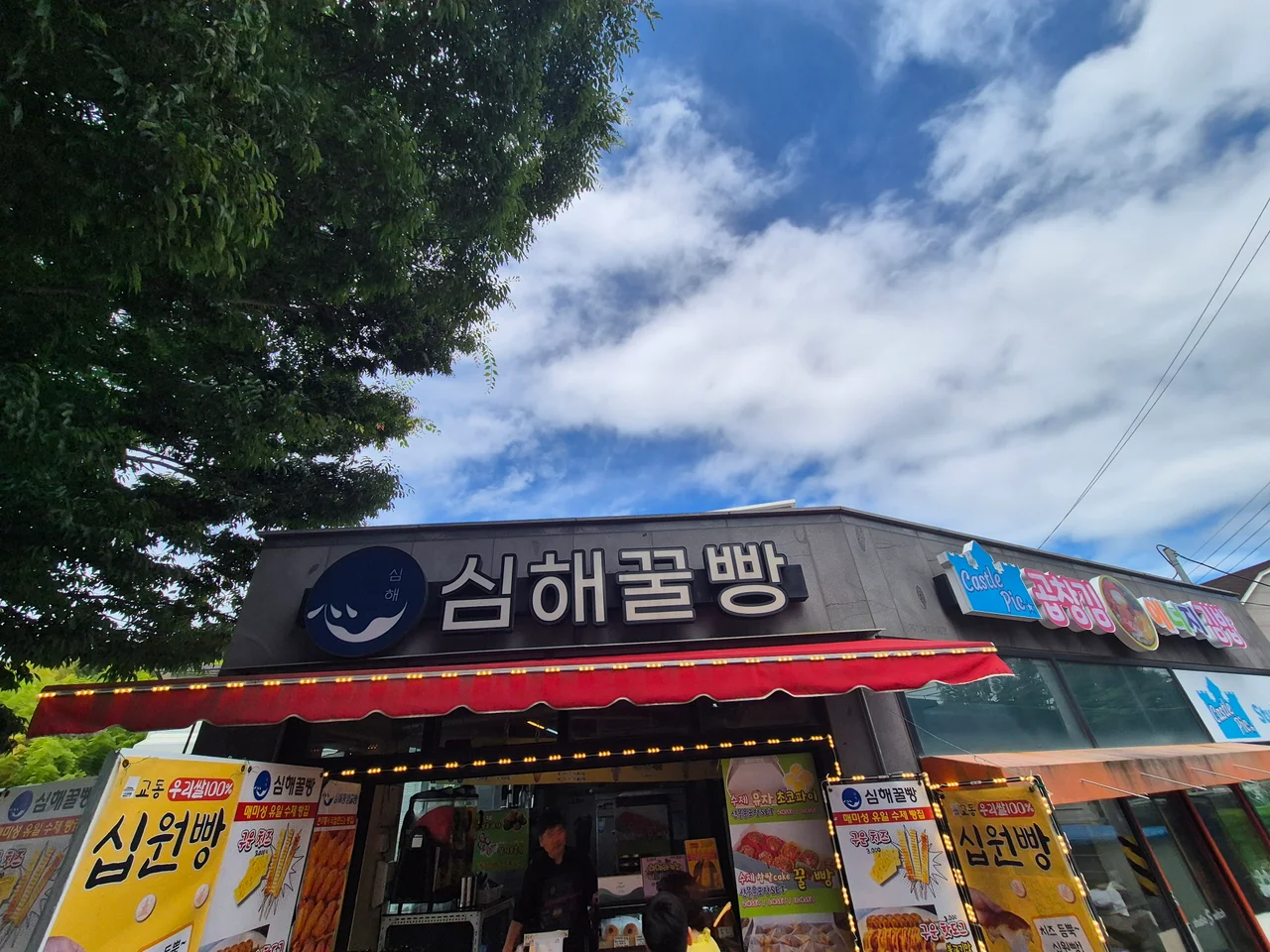 맑고 파란 하늘 아래 선명하고 돋보이는 심해꿀빵 매장의 깔끔한 간판 외관