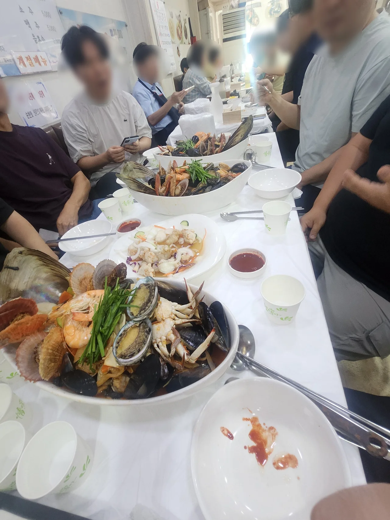 일행들과 함께 테이블 가득 차려진 풍성한 해물 요리를 즐기고 있는 활기찬 식사 현장