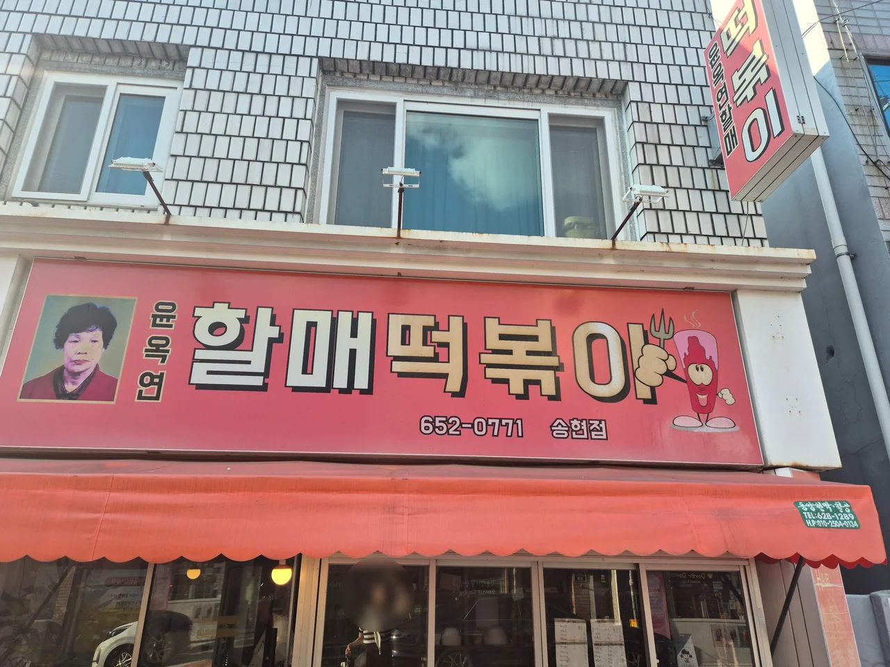 빨간색 간판에 할머니 얼굴 그림이 그려진 윤옥연할매떡볶이 송현점 외관