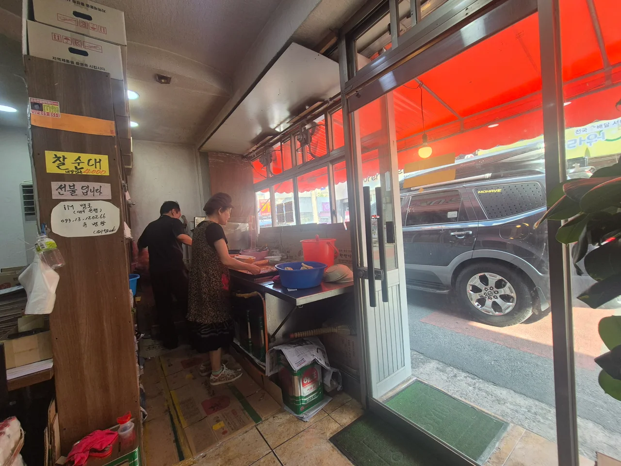 주방 안쪽에서 분식을 조리하는 직원들과 열려 있는 유리문 입구 풍경
