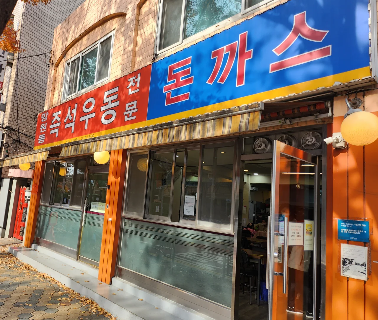 망원동즉석우동 본점의 주황색 건물 외관과 파란색 돈까스 간판