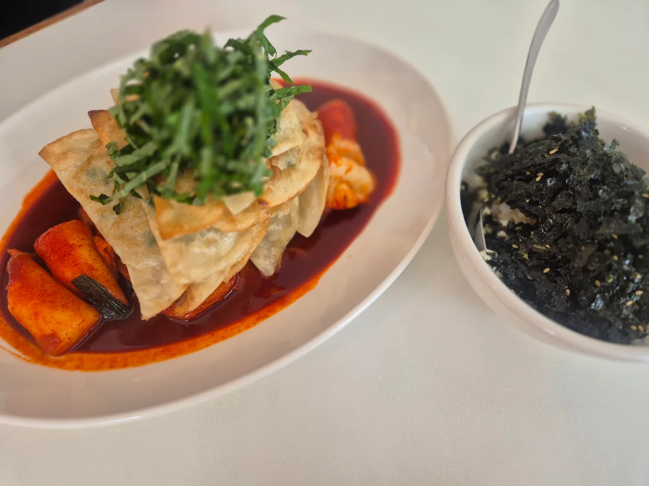 붉은 떡볶이 위에 납작만두와 잘게 썬 깻잎이 올라간 모습