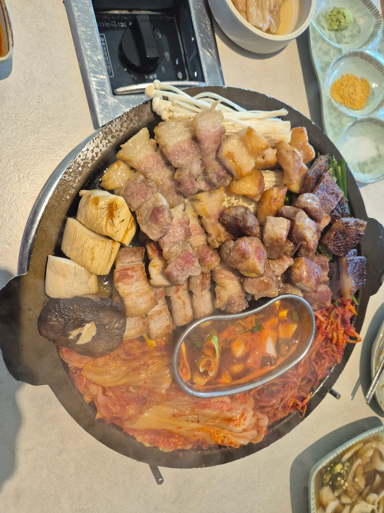 돌판 위에서 노릇하게 구워진 삼겹살과 목살, 김치, 멜젓 상차림