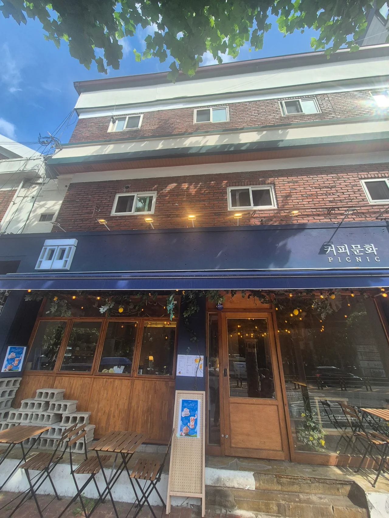 네이비색 어닝과 우드 톤 창문이 돋보이는 카페 건물 외관 정면
