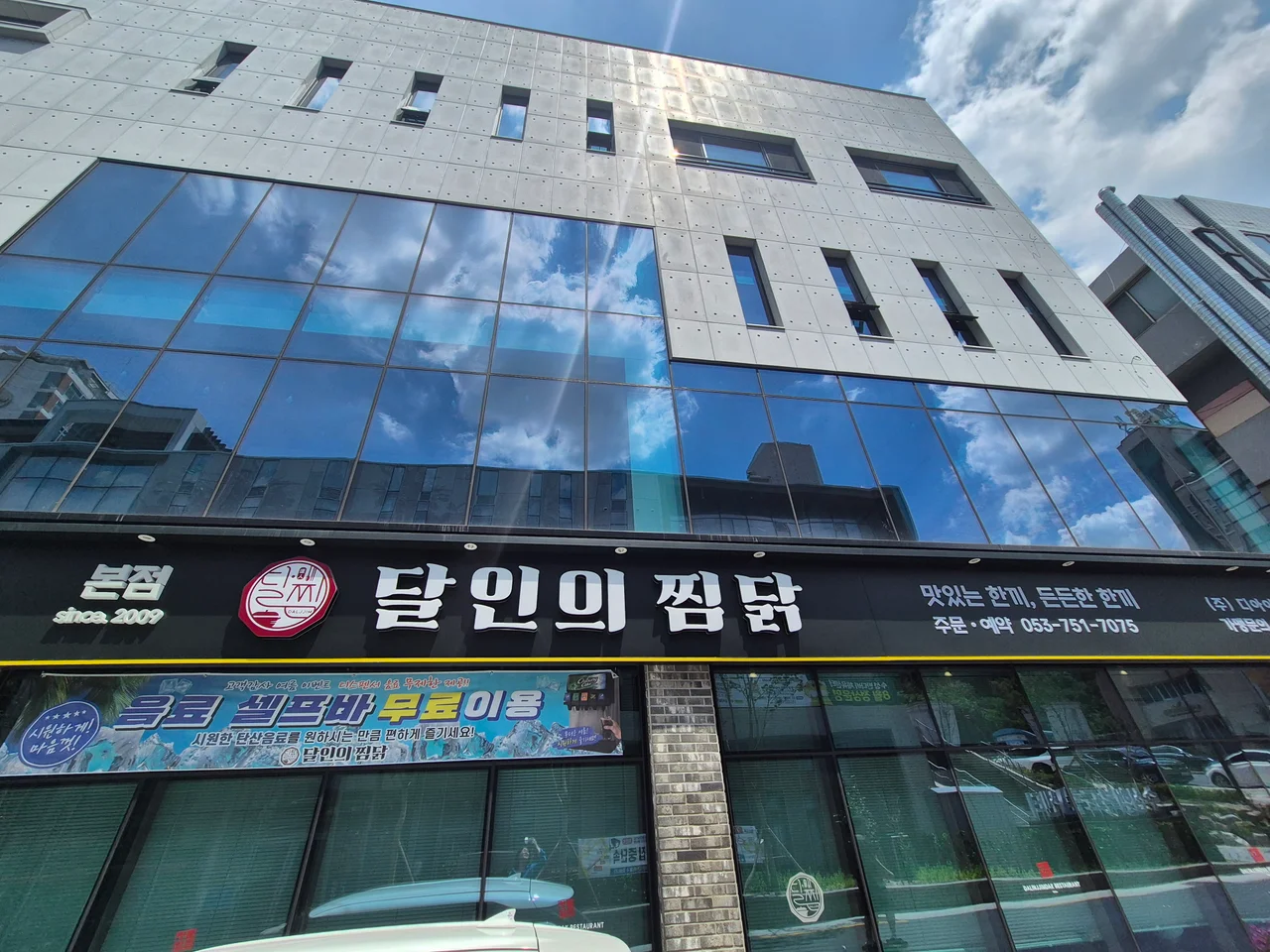 달인의찜닭 본점 건물 전면 유리에 반사된 하늘과 매장 간판