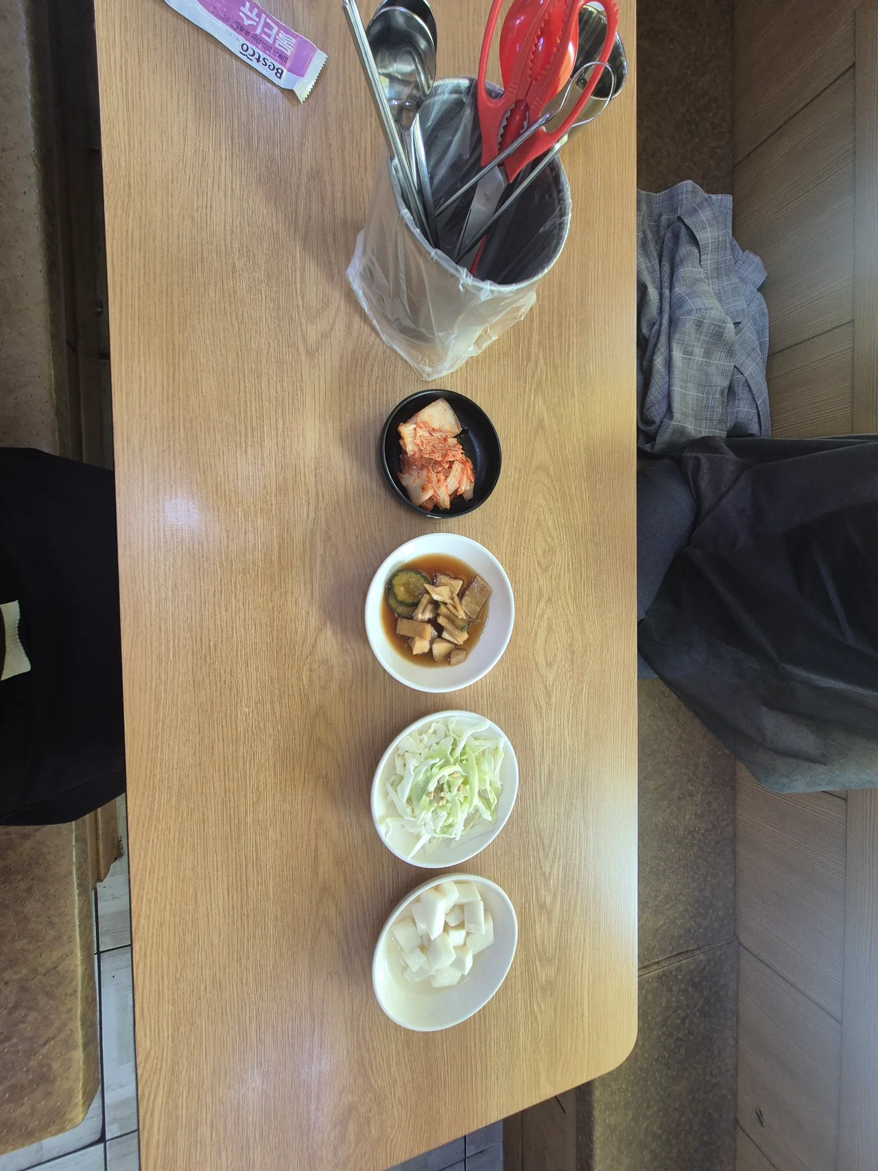 테이블에 정갈하게 세팅된 김치, 양파장아찌, 샐러드, 치킨무 반찬