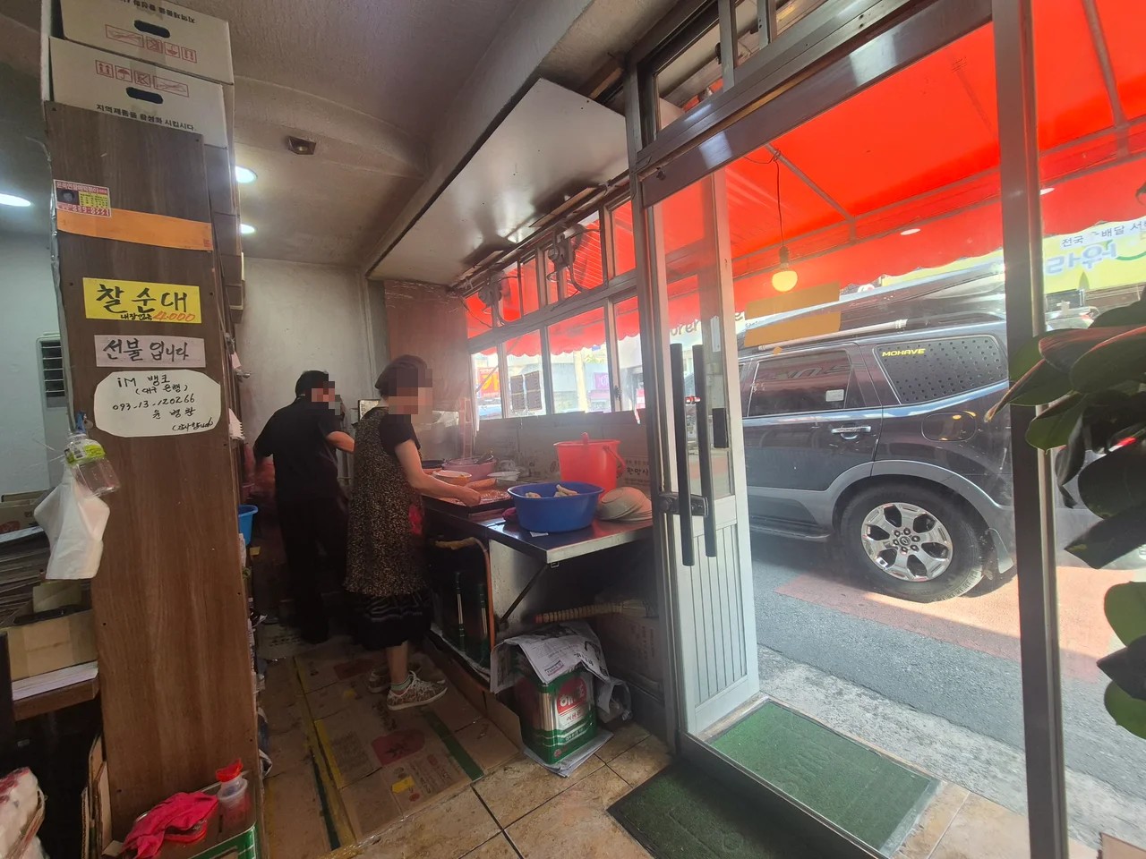주방 안쪽에서 분식을 조리하는 직원들과 열려 있는 유리문 입구 풍경